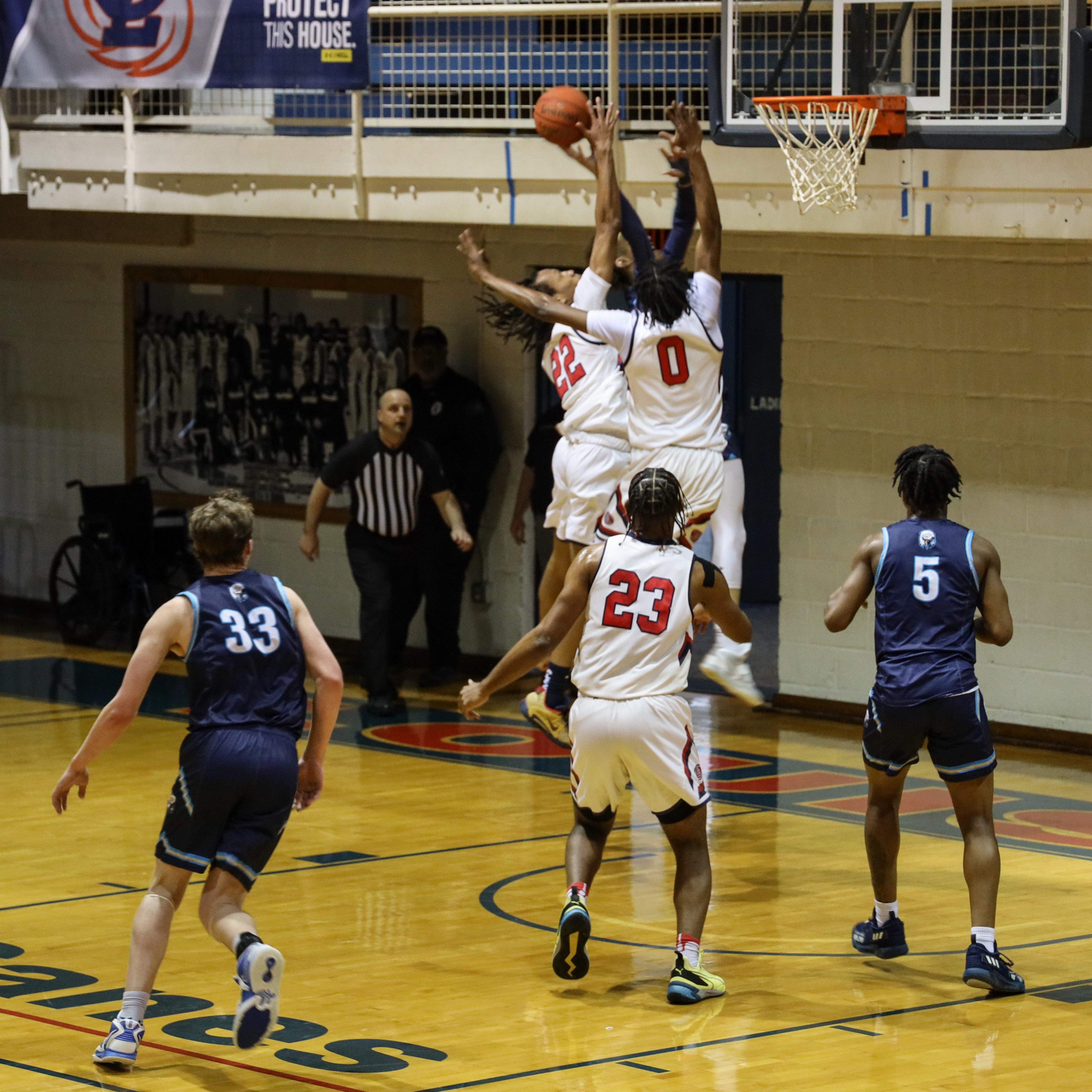 Men's Basketball players go up to block a lay-up.